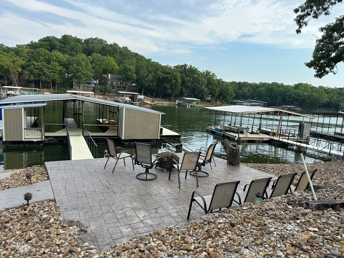 A tranquil lakefront dock with comfortable seating directly over the water, perfect for relaxing or fishing. The dock overlooks calm water and is surrounded by lush trees, inviting guests to enjoy the lakeside atmosphere at any time of day.