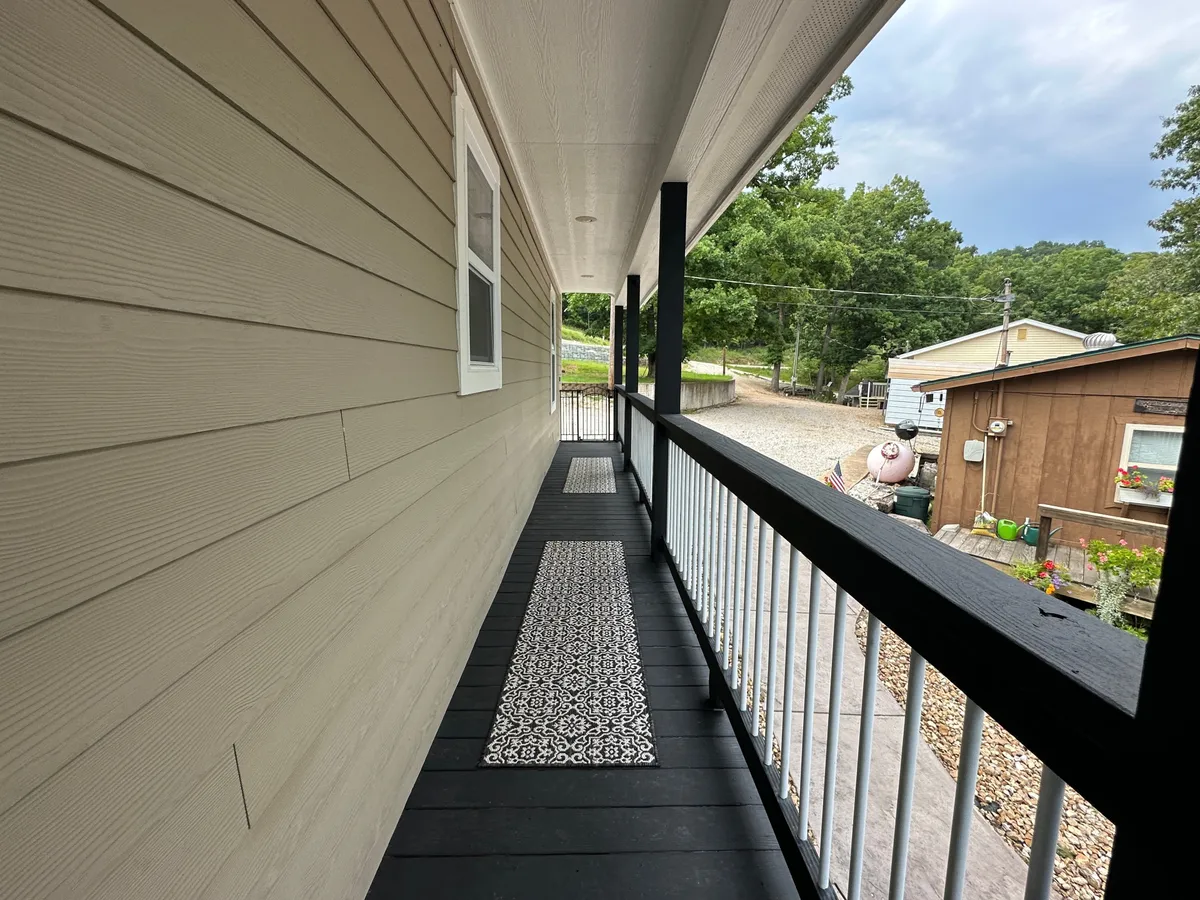 A welcoming exterior porch area with a patterned runner mat, sturdy railing, and a scenic view of greenery. The setting suggests a transitional space from the home to the outdoors, suitable for preparing for pet outings or relaxing after a walk.
