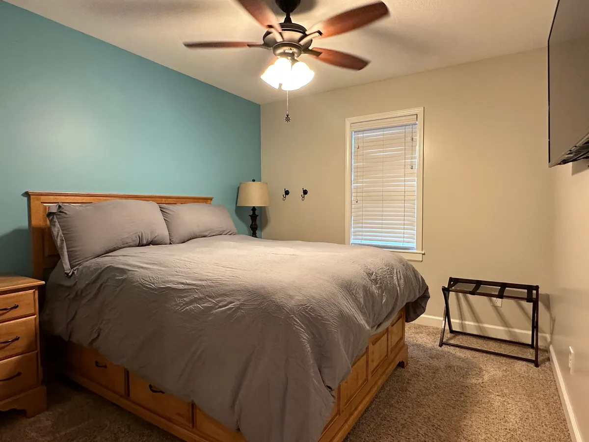 A calm, uncluttered bedroom with a comfortable bed, bedside lamp, large window flooding the space with natural light, and a ceiling fan overhead, all combining to create a soothing ambiance perfect for rest.