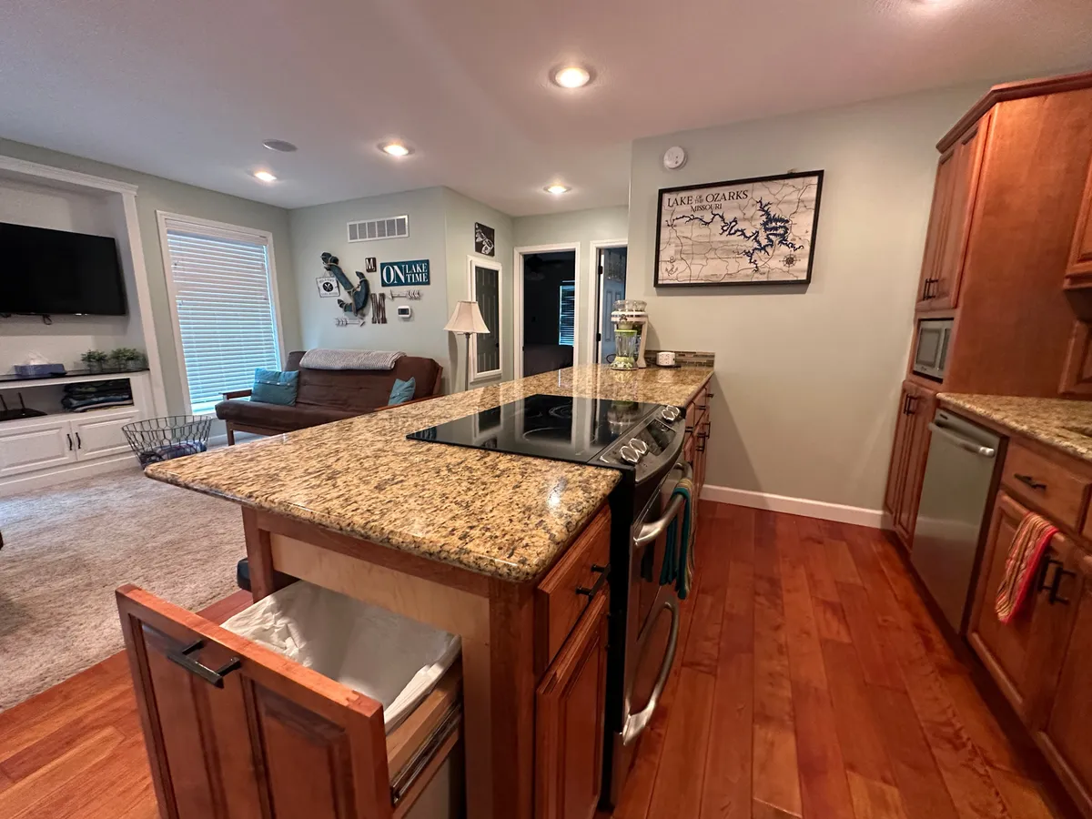 A modern kitchen with a large granite-topped island, stylish appliances, and a view of a welcoming living area in the background. The space is open for entertaining, cooking, and family gatherings, suggesting both convenience and a sense of security.
