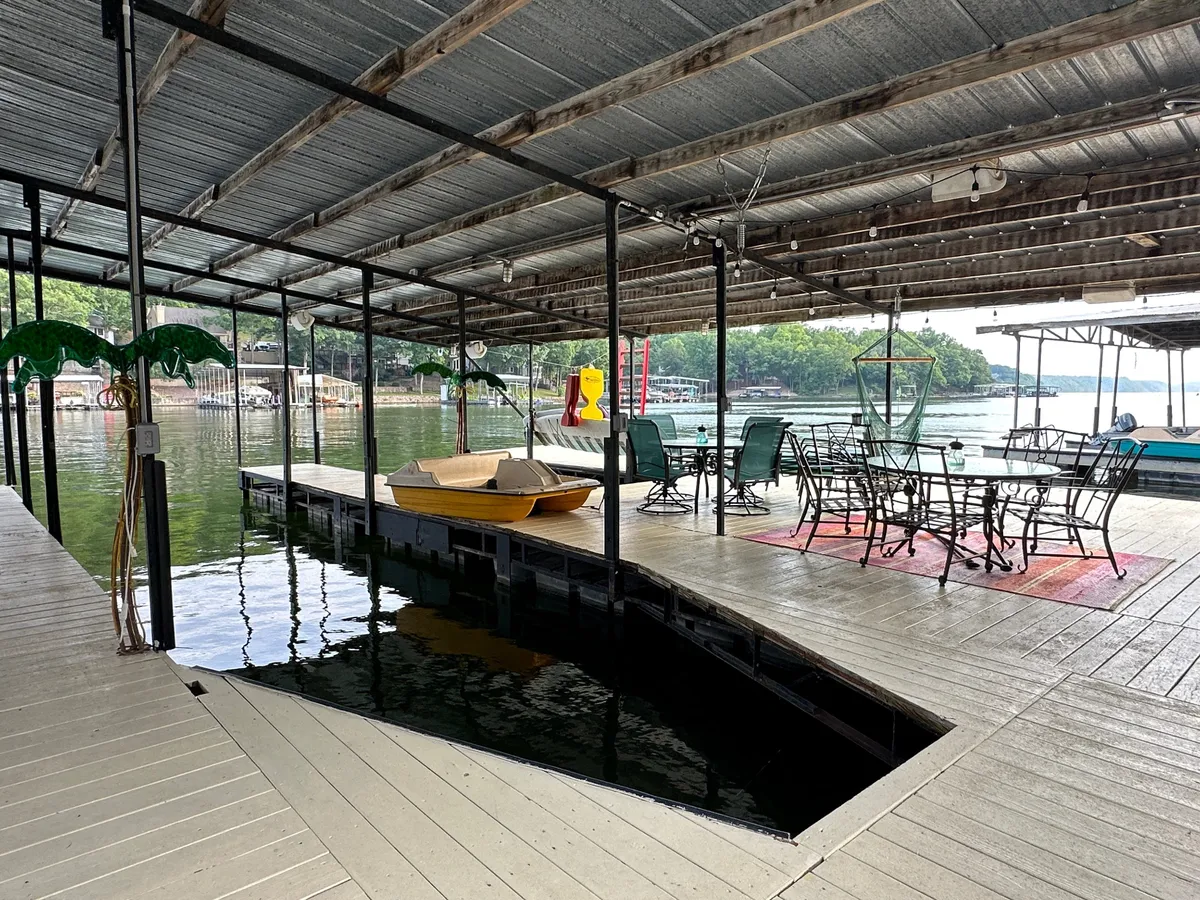 This image features a dock extending over the water, a yellow paddle boat, an outdoor dining set, and tranquil lake views. Green decorative elements add a pop of color, and the setting communicates both relaxation and the excitement of water activities.