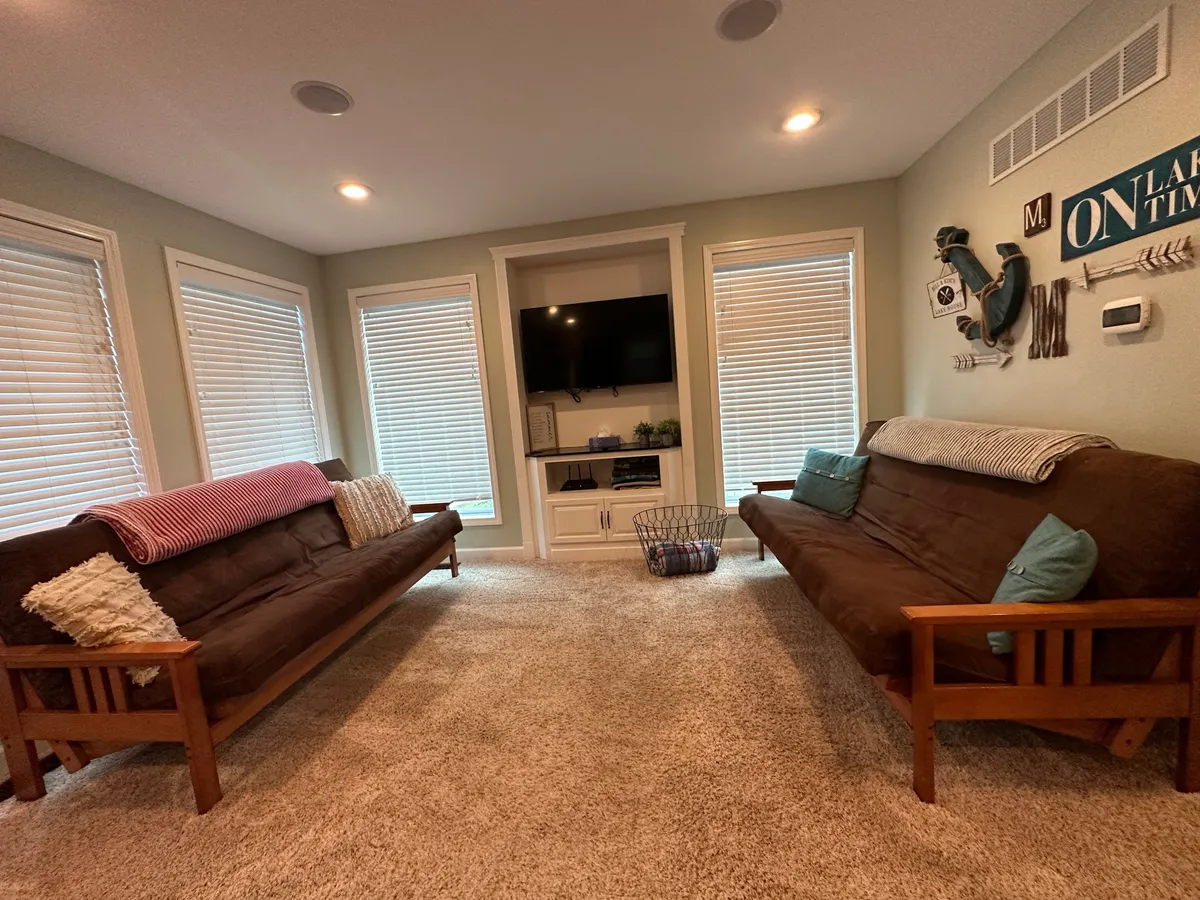A cozy living room featuring two futons, a TV unit with a large television, and decorative wall art. The space is arranged to promote comfortable family gatherings, game nights, and relaxed socializing.