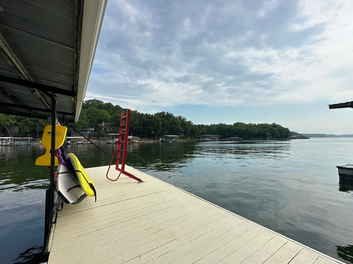 A dock with a striking red ladder, multiple surfboards, and views of the water and distant shoreline. The dock is designed for swimming, fishing, and launching water activities, with vibrant elements conveying a sense of fun and adventure.